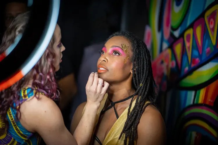 Makeup artist applying colorful editorial makeup to a Black woman during a live event in St. Petersburg